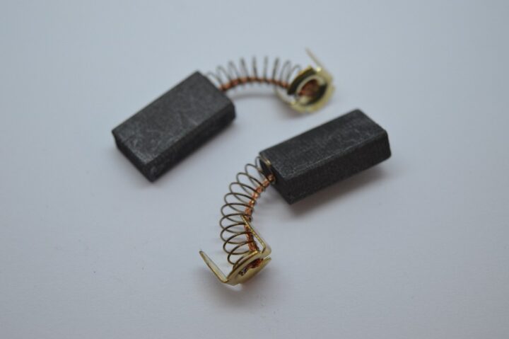 Two carbon motor brushes with copper springs resting on a white surface, shown from above