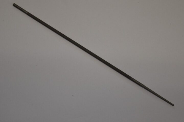Slender metal rod lying diagonally on a light surface, with threaded ends visible at both ends.