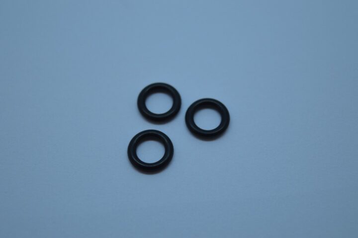 Three black rubber O-rings arranged on a pale blue surface, viewed from above.