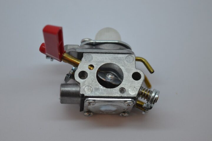 Close-up of a small metal carburetor with a red throttle lever and brass fuel lines visible.