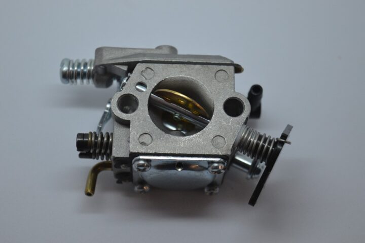 Metal carburetor component with intake bore, screws and linkages visible on a light background—likely a small engine part.