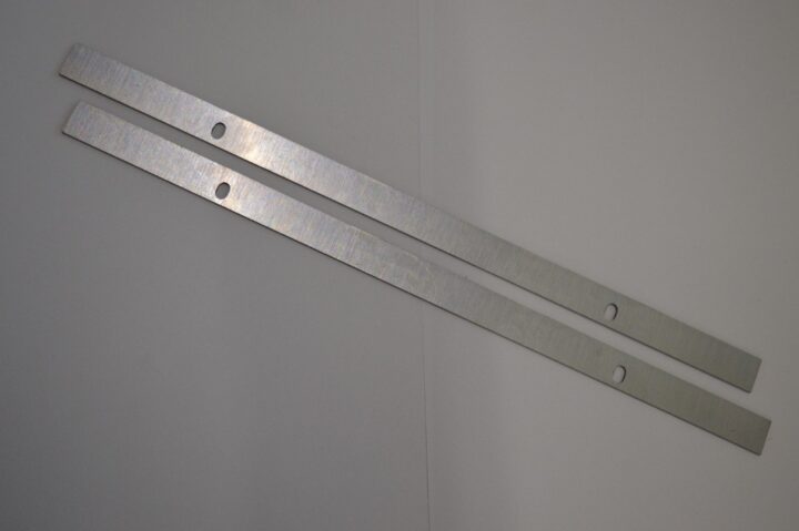 Two long, flat metal strips with evenly spaced circular holes lying diagonally on a light surface.